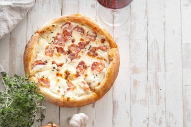 Beyaz ahşap sıkıntılı masada şarap kadehi ile servis domuz pastırması ve kekik ile peynir ile pişmiş pizza üst görünümü