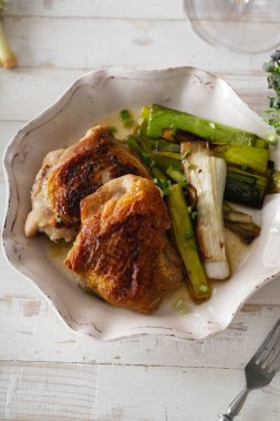 Beyaz ahşap masada kase de pırasa ve şarap sosu ile kavrulmuş deri tavuk uyluk