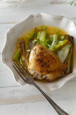 Beyaz ahşap masada kase de pırasa ve şarap sosu ile kavrulmuş deri tavuk uyluk