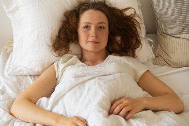 Pijama giyen genç ve mutlu bir kadın yatak odasında uyanıyor. 