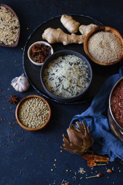 Mavi arka plan üzerinde kaselerde baharat ile pirinç ve tahıl çeşitleri 