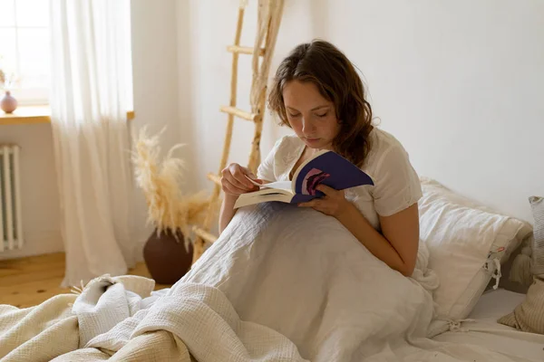 Sabahın Erken Saatlerinde Yatakta Oturmuş Roman Okuyan Genç Bir Kadın — Stok fotoğraf