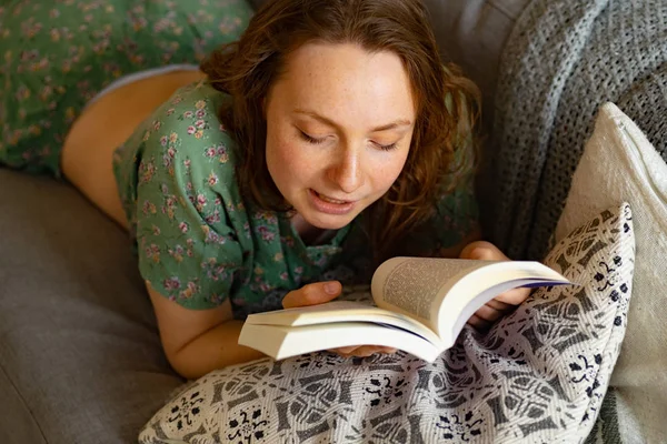 Jovem Mulher Lendo Livro Enquanto Deitado Sofá Casa — Fotografia de Stock