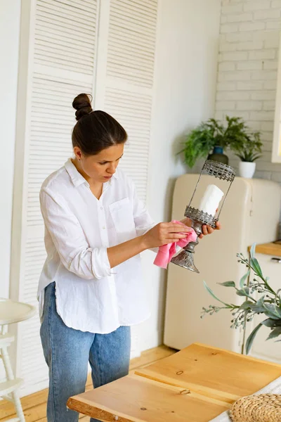 Young woman in casual clothes cleaning dust at kitchen