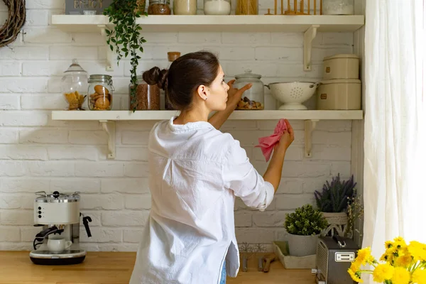 Young woman in casual clothes cleaning dust at kitchen