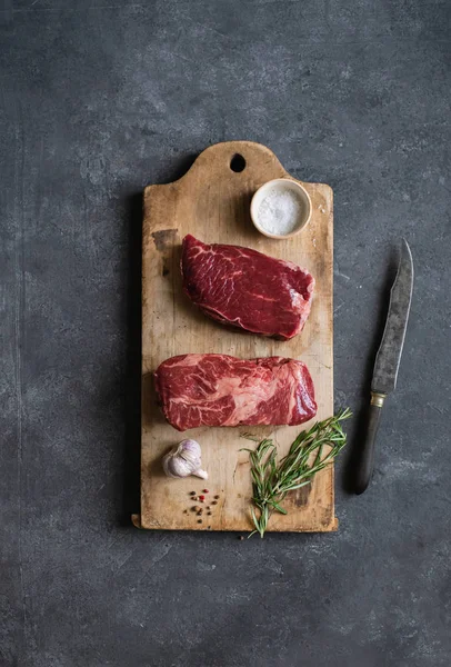 Sarımsak ile biberiye ve deniz tuzu ile vintage kesme tahtası üzerinde Çiğ siyah angus prime sığır biftek 