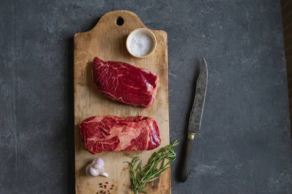 Sarımsak ile biberiye ve deniz tuzu ile vintage kesme tahtası üzerinde Çiğ siyah angus prime sığır biftek 