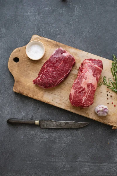 Sarımsak ile biberiye ve deniz tuzu ile vintage kesme tahtası üzerinde Çiğ siyah angus prime sığır biftek 