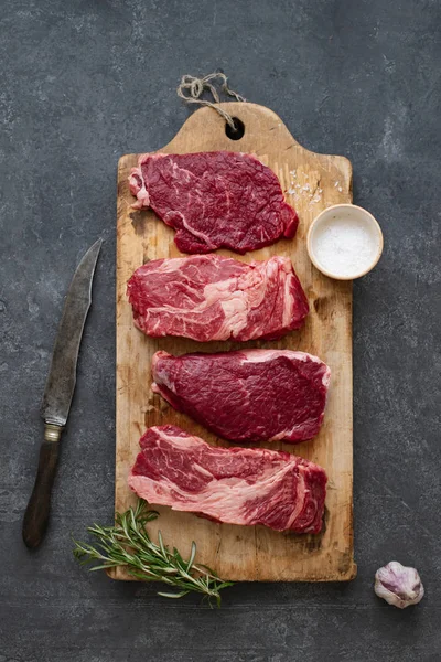 Sarımsak ile biberiye ve deniz tuzu ile vintage kesme tahtası üzerinde Çiğ siyah angus prime sığır biftek 