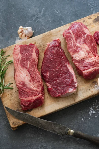 Sarımsak ile biberiye ve deniz tuzu ile vintage kesme tahtası üzerinde Çiğ siyah angus prime sığır biftek 