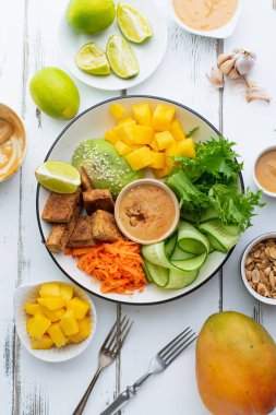 beyaz ahşap masa üzerinde tofu ve tatlı fıstık ezmesi ile mango ve avokado sağlıklı yaz taze salata ile plaka 