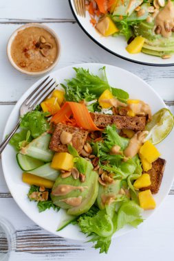 beyaz ahşap masa üzerinde tofu ve tatlı fıstık ezmesi ile mango ve avokado sağlıklı yaz taze salata ile plaka 