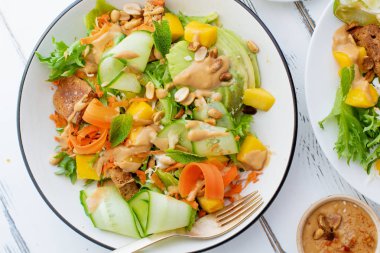 beyaz ahşap masa üzerinde tofu ve tatlı fıstık ezmesi ile mango ve avokado sağlıklı yaz taze salata ile plaka 