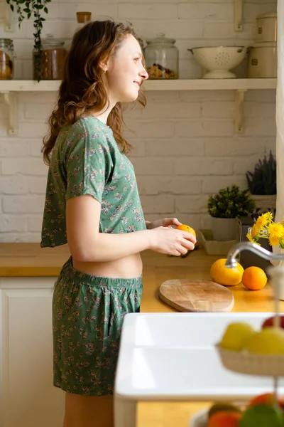 Junge Frau Schält Frische Orange Während Sie Der Küche Steht — Stockfoto