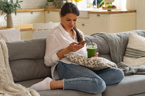 Evde Kanepede Otururken Yeşil Smoothie Içme Akıllı Telefona Bakarak Genç — Stok fotoğraf