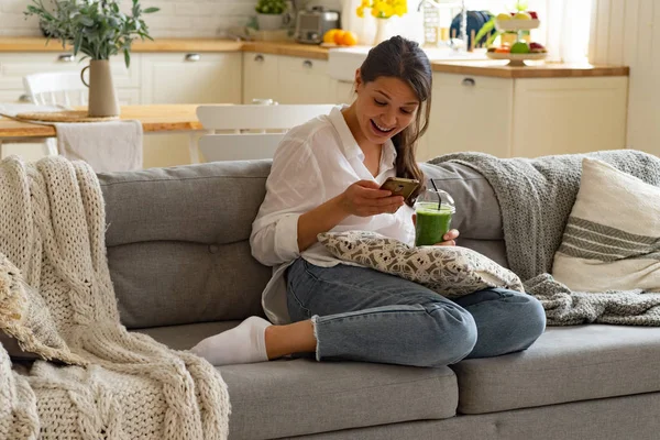 Akıllı Telefon Kullanırken Gülümseyen Mutlu Kadın Evde Yeşil Smoothie Fincan — Stok fotoğraf