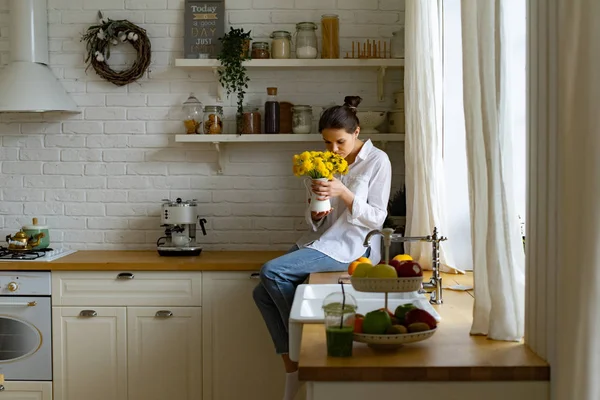 Młoda Kobieta Trzyma Wazon Jasnym Żółtym Bukiet Kwiatów Siedząc Stole — Zdjęcie stockowe