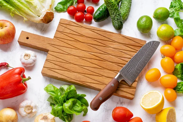 top view of vegetables with salad leaves and greens around wooden cutting board with knife, ingredients for cooking ragout 