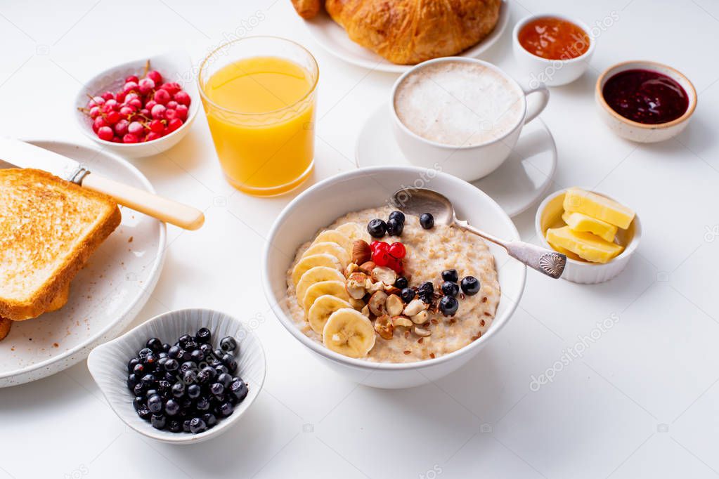 bowl with oatmeal and berries with croissants and toasts on plates and coffee with orange juice in cups, Breakfast concept 