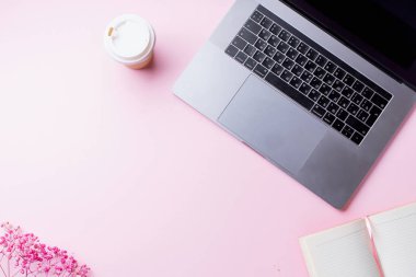 dizüstü bilgisayar ve kahve ile kadın blogger işyeri pembe arka plan üzerinde not defteri ile fincan gitmek. Üstte görüntü  