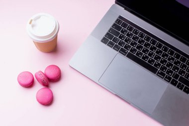 dizüstü bilgisayar ve kahve ile kadın blogger işyeri pembe arka plan üzerinde macaroons ile fincan gitmek. Üstte görüntü  