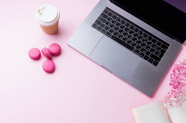 dizüstü bilgisayar ve kahve ile kadın blogger işyeri pembe arka plan üzerinde not defteri ve macaroons ile fincan gitmek. Üstte görüntü  