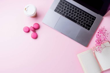 dizüstü bilgisayar ve kahve ile kadın blogger işyeri pembe arka plan üzerinde not defteri ve macaroons ile fincan gitmek. Üstte görüntü  