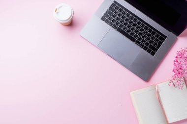 dizüstü bilgisayar ve kahve ile kadın blogger işyeri pembe arka plan üzerinde not defteri ile fincan gitmek. Üstte görüntü  