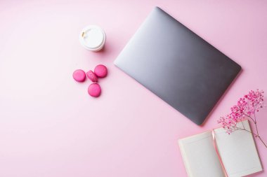 dizüstü bilgisayar ve kahve ile kadın blogger işyeri pembe arka plan üzerinde not defteri ve macaroons ile fincan gitmek. Üstte görüntü  