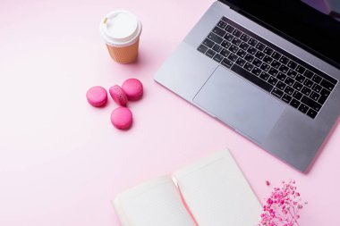 dizüstü bilgisayar ve kahve ile kadın blogger işyeri pembe arka plan üzerinde not defteri ve macaroons ile fincan gitmek. Üstte görüntü  