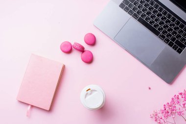 dizüstü bilgisayar ve kahve ile kadın blogger işyeri pembe arka plan üzerinde not defteri ve macaroons ile fincan gitmek. Üstte görüntü  