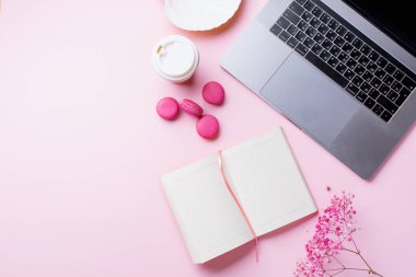 dizüstü bilgisayar ve kahve ile kadın blogger işyeri pembe arka plan üzerinde not defteri ve macaroons ile fincan gitmek. Üstte görüntü  