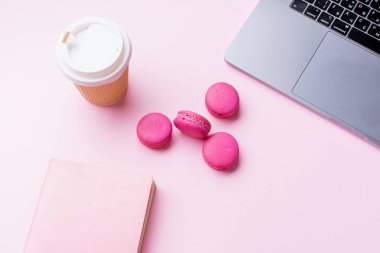 dizüstü bilgisayar ve kahve ile kadın blogger işyeri pembe arka plan üzerinde not defteri ve macaroons ile fincan gitmek. Üstte görüntü  