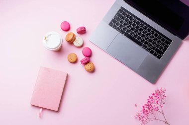 dizüstü bilgisayar ve kahve ile kadın blogger işyeri pembe arka plan üzerinde not defteri ve macaroons ile fincan gitmek. Üstte görüntü  