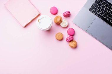 dizüstü bilgisayar ve kahve ile kadın blogger işyeri pembe arka plan üzerinde not defteri ve macaroons ile fincan gitmek. Üstte görüntü  