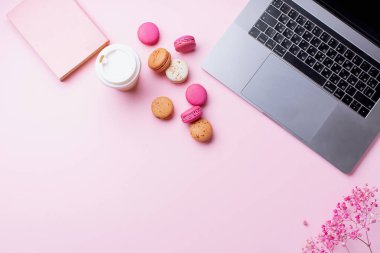 dizüstü bilgisayar ve kahve ile kadın blogger işyeri pembe arka plan üzerinde not defteri ve macaroons ile fincan gitmek. Üstte görüntü  