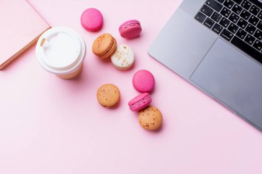 dizüstü bilgisayar ve kahve ile kadın blogger işyeri pembe arka plan üzerinde not defteri ve macaroons ile fincan gitmek. Üstte görüntü  