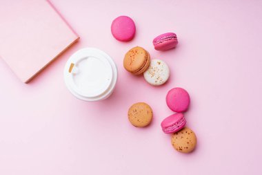 kahve ile kadın blogger işyeri pembe arka plan üzerinde macaroons ile fincan ve not defteri gitmek. Üstte görüntü  