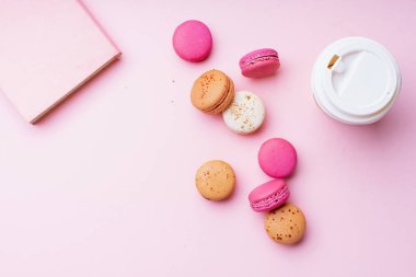 kahve ile kadın blogger işyeri pembe arka plan üzerinde macaroons ile fincan ve not defteri gitmek. Üstte görüntü  