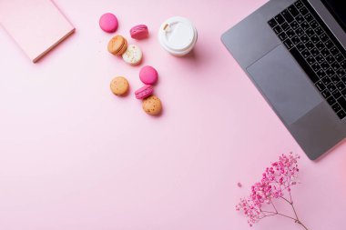 dizüstü bilgisayar ve kahve ile kadın blogger işyeri pembe arka plan üzerinde not defteri ve macaroons ile fincan gitmek. Üstte görüntü  
