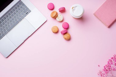 dizüstü bilgisayar ve kahve ile kadın blogger işyeri pembe arka plan üzerinde not defteri ve macaroons ile fincan gitmek. Üstte görüntü  