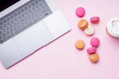 dizüstü bilgisayar ve kahve ile kadın blogger işyeri pembe arka plan üzerinde macaroons ile fincan gitmek. Üstte görüntü  