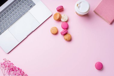 dizüstü bilgisayar ve kahve ile kadın blogger işyeri pembe arka plan üzerinde not defteri ve macaroons ile fincan gitmek. Üstte görüntü  