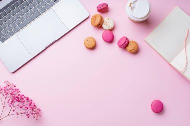 dizüstü bilgisayar ve kahve ile kadın blogger işyeri pembe arka plan üzerinde not defteri ve macaroons ile fincan gitmek. Üstte görüntü  