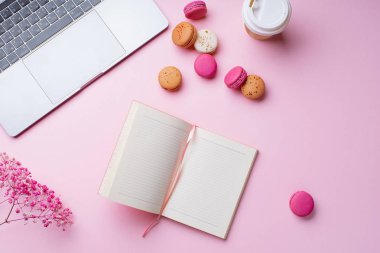 dizüstü bilgisayar ve kahve ile kadın blogger işyeri pembe arka plan üzerinde not defteri ve macaroons ile fincan gitmek. Üstte görüntü  