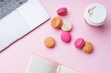 dizüstü bilgisayar ve kahve ile kadın blogger işyeri pembe arka plan üzerinde not defteri ve macaroons ile fincan gitmek. Üstte görüntü  