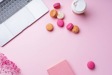 dizüstü bilgisayar ve kahve ile kadın blogger işyeri pembe arka plan üzerinde not defteri ve macaroons ile fincan gitmek. Üstte görüntü  