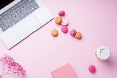 dizüstü bilgisayar ve kahve ile kadın blogger işyeri pembe arka plan üzerinde not defteri ve macaroons ile fincan gitmek. Üstte görüntü  