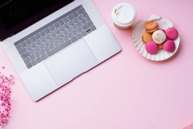 dizüstü bilgisayar ve kahve ile kadın blogger işyeri pembe arka plan üzerinde macaroons ile fincan gitmek. Üstte görüntü  
