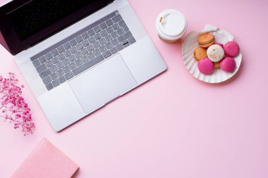 dizüstü bilgisayar ve kahve ile kadın blogger işyeri pembe arka plan üzerinde not defteri ve macaroons ile fincan gitmek. Üstte görüntü  